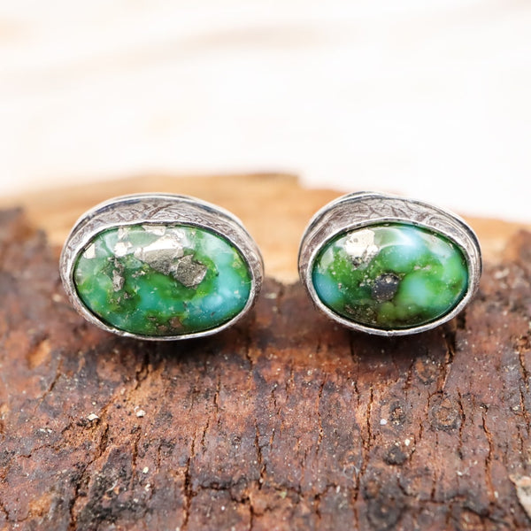 A close up of two mismatched green sonoran gold turquoise earring studs with leaf patterned bezels. 