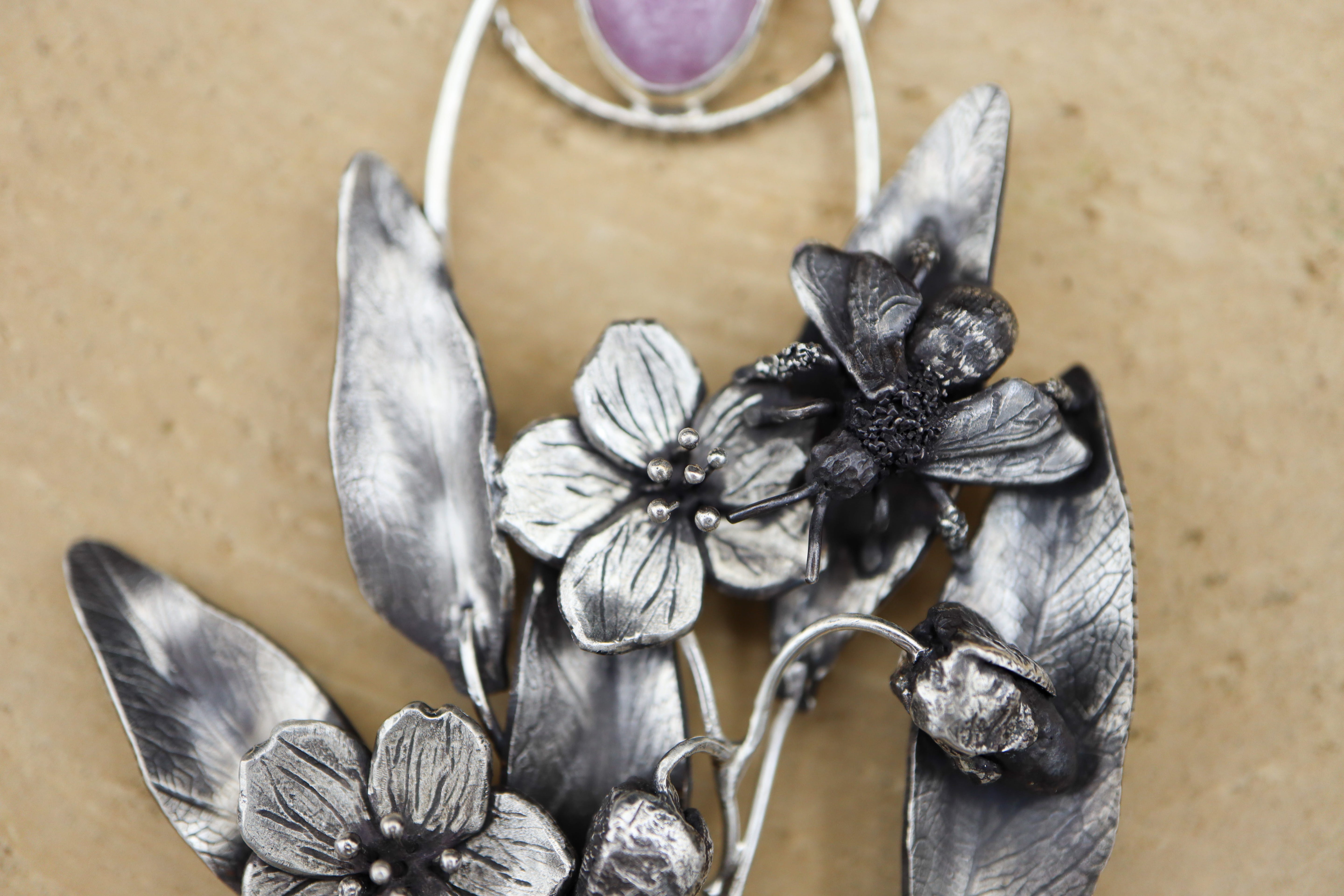 A close up photo of the handmade spring beauty mining bee on the flower necklace. It is shown on a piece of tan wood.
