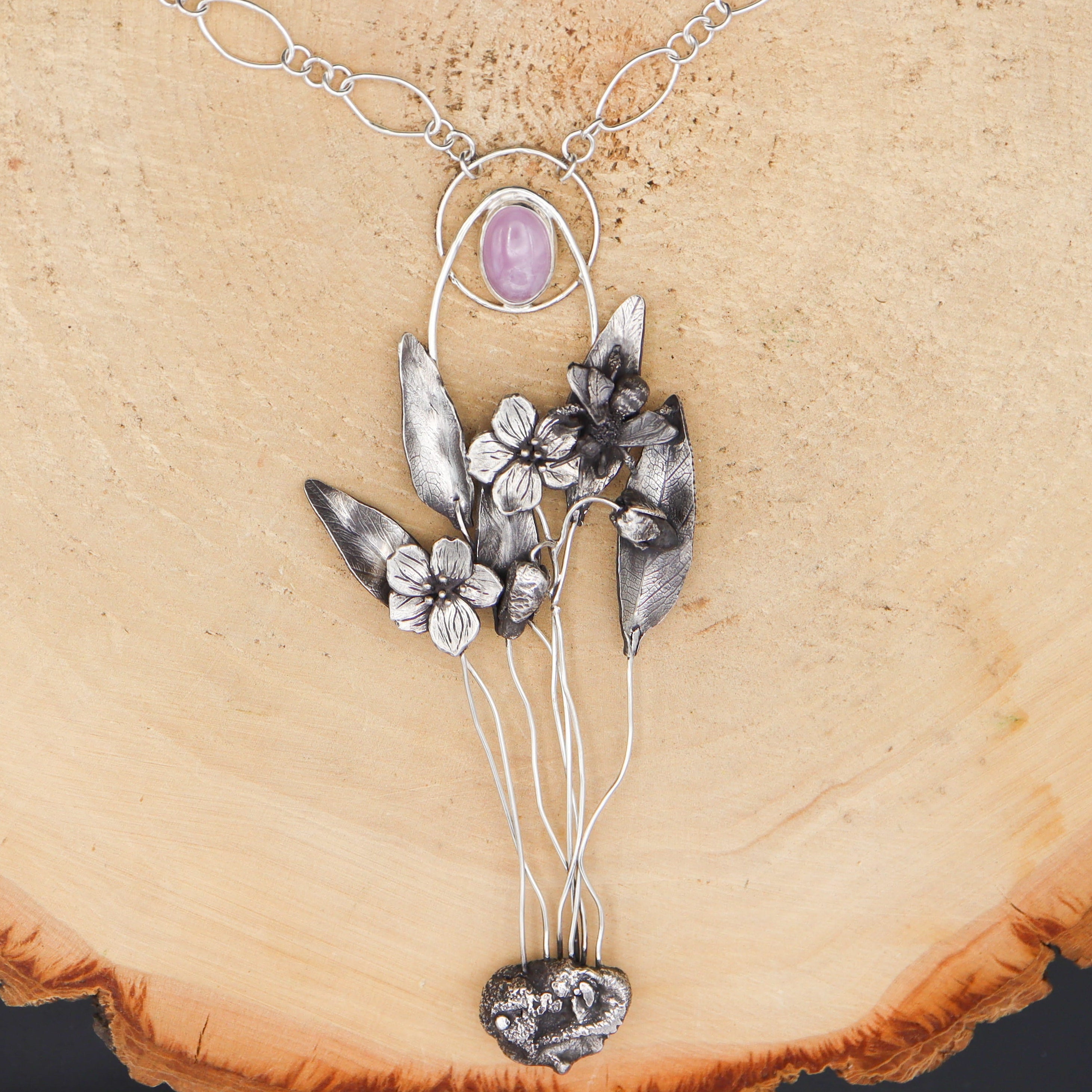 Silver necklace with spring beauty wildflowers and a tiny mining bee pendant on a wooden surface