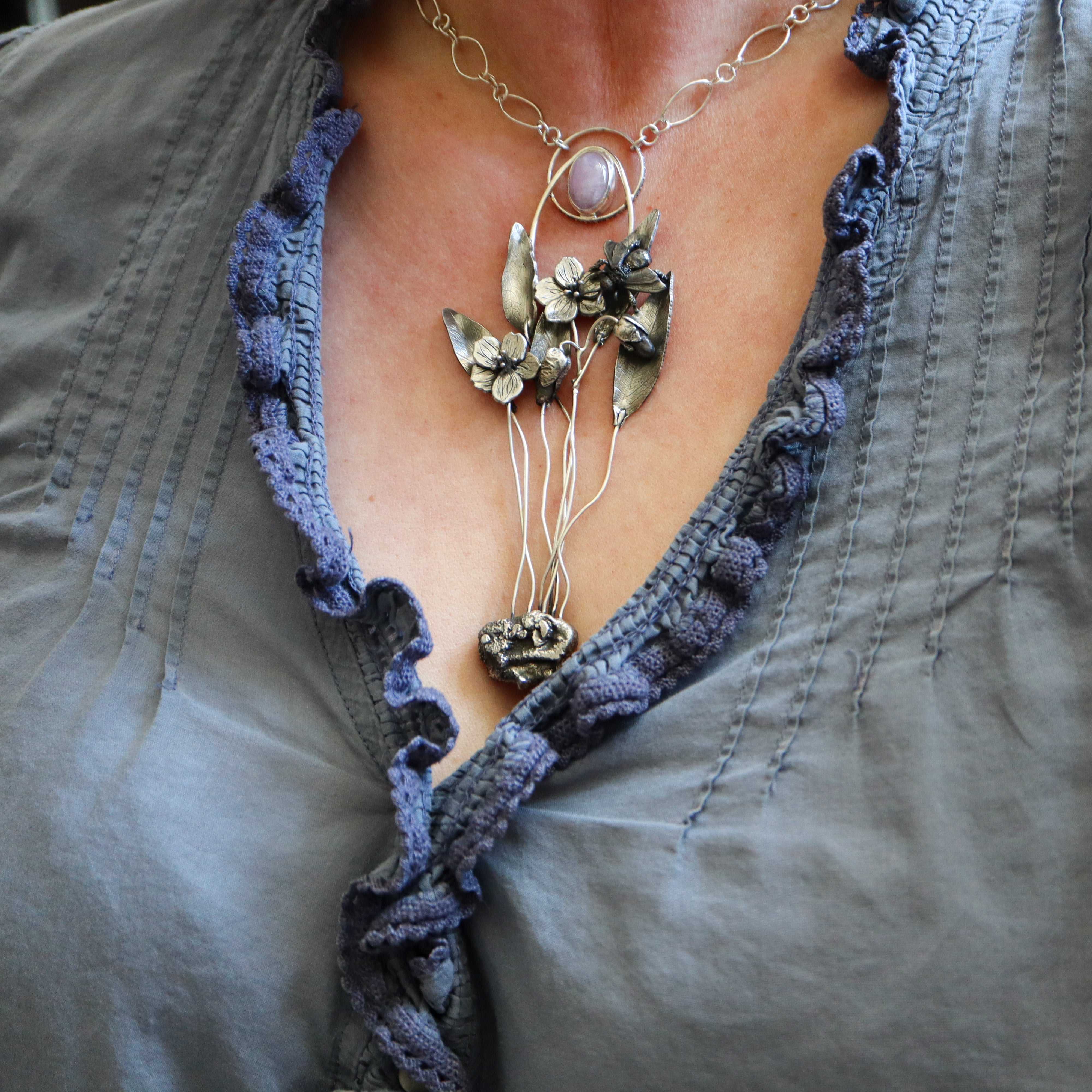 A woman in a purple blouse is shown wearing the spring beauty mining bee necklace. 
