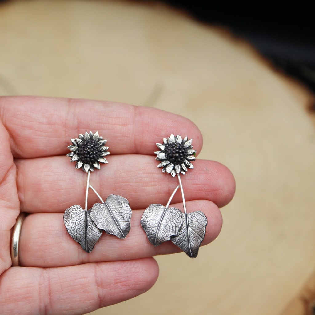 A hand is shown holding the handmade sterling silver sunflower stud dangle earrings.