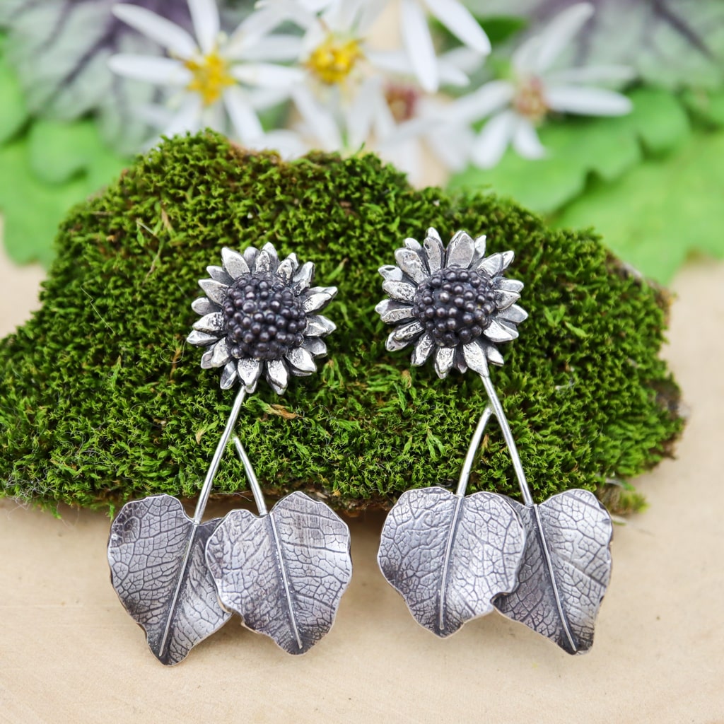 Sterling silver sunflower dangle earrings are shown on a piece of dark green moss. 
