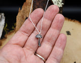 A hand is shown hold the tiny sterling silver mushroom necklace. It is about 1/2 inch tall. 