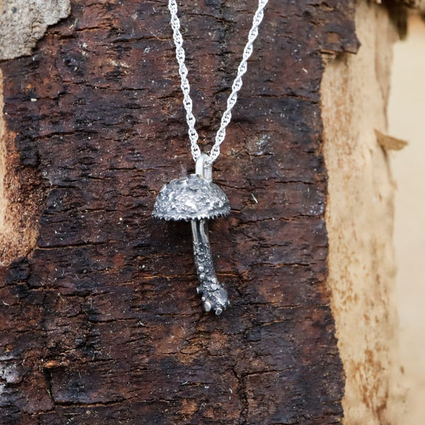 Sterling silver handmade tiny mushroom necklace. It is made with a lot of texture looking like it just came from the soil. It is about 1/2 inch tall and comes on an 18 inch long sterling silver necklace. The pendant is shown on a dark brown piece of wood.