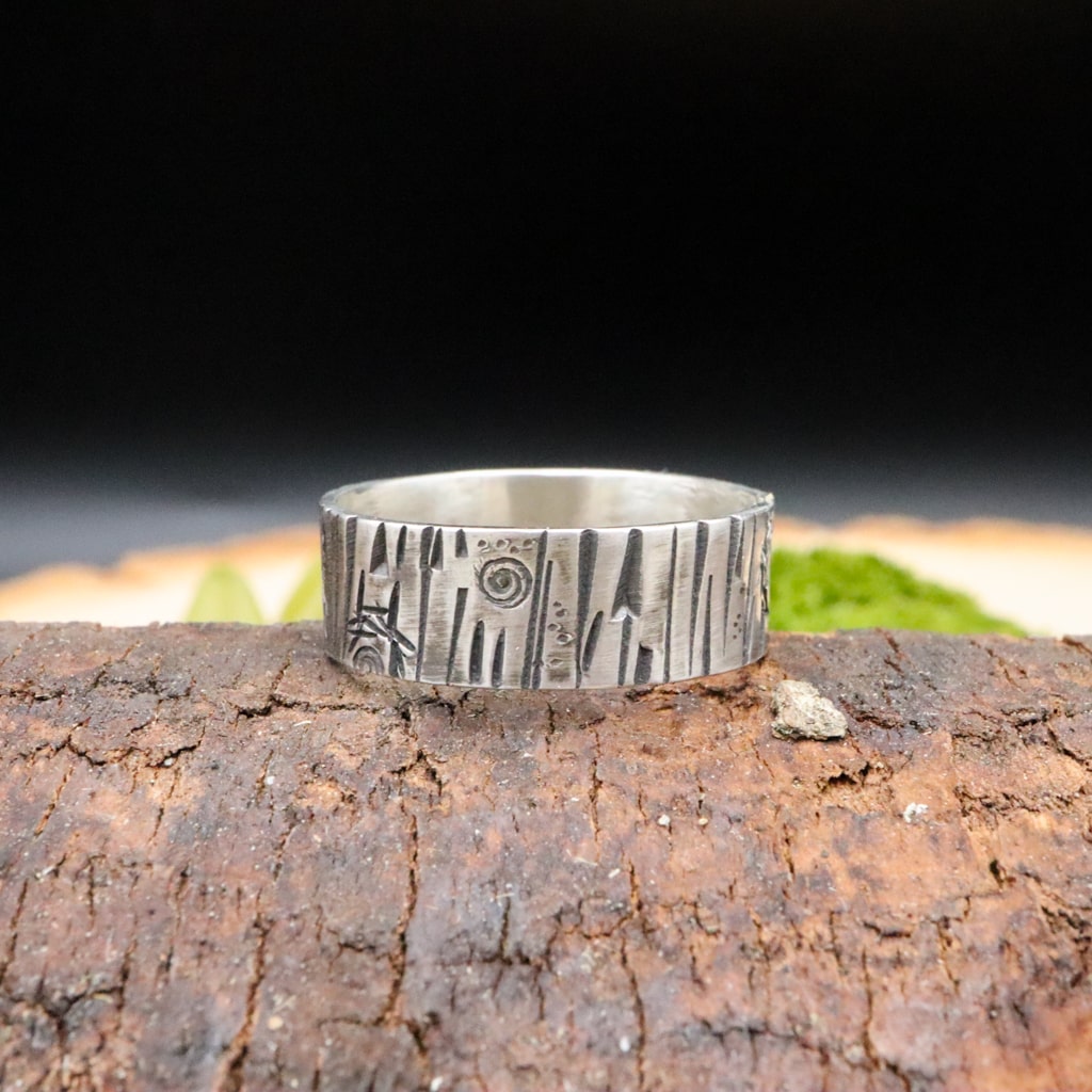 A sterling silver handmade tree bark textured ring is shown on a piece of dark brown wood. 