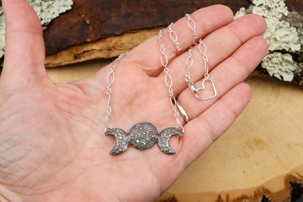 A hand is shown holding the triple moon goddess necklace made from sterling silver. 