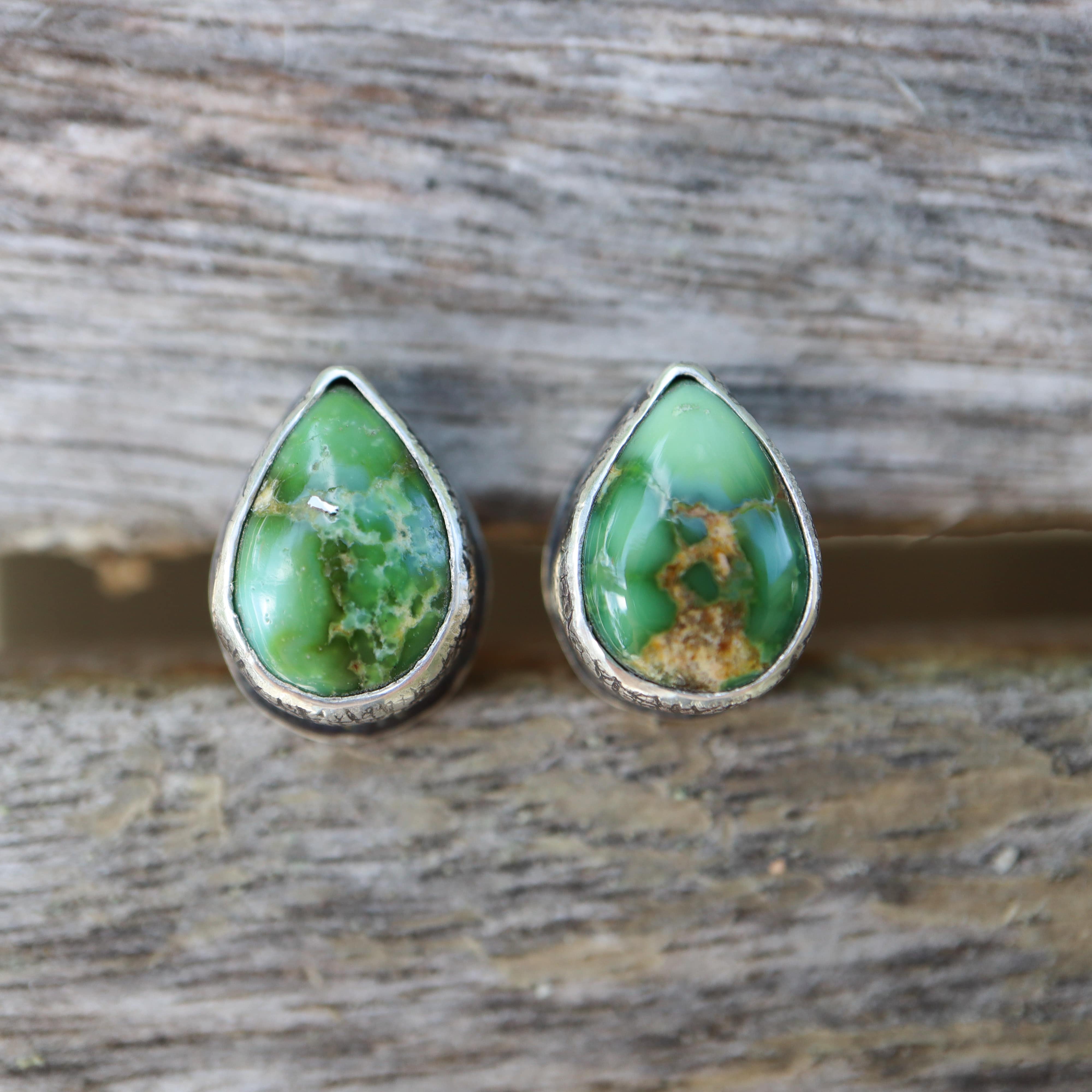 Teardrop-shaped green turquoise stone earrings on a wooden surface