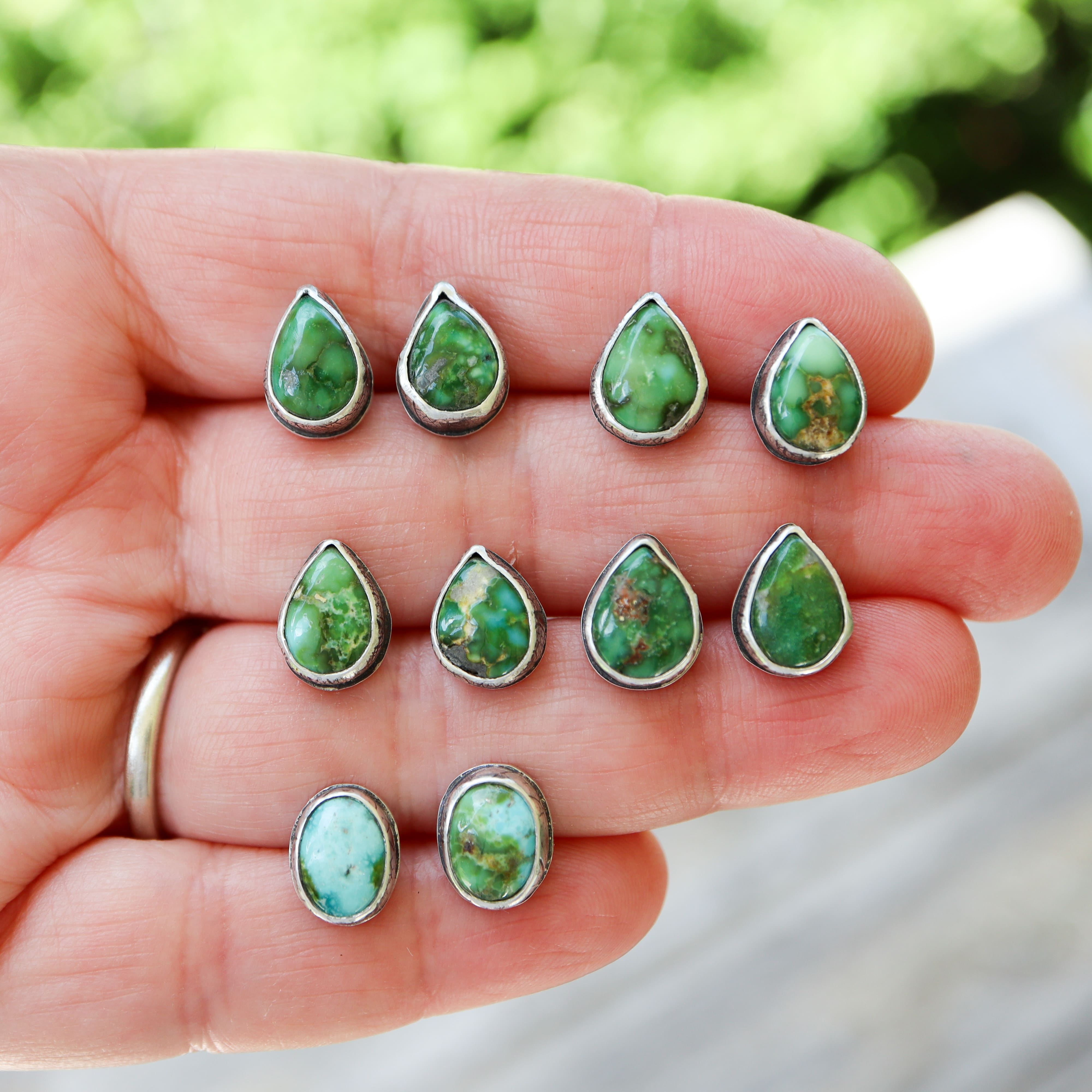 Green teardrop turquoise earrings held in a hand with a blurred green background