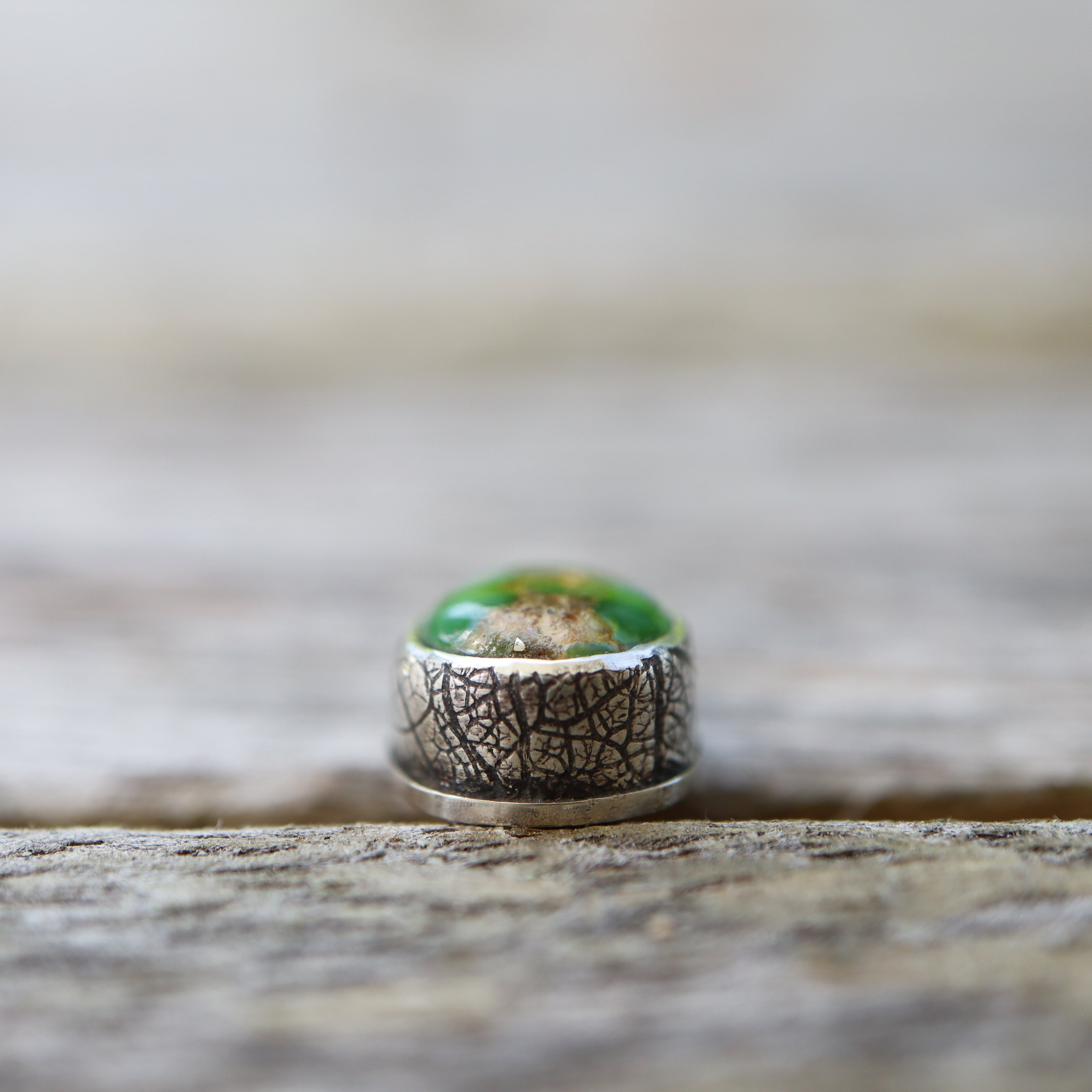 Silver earring with green turquoise stone on a wooden surface