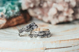 A pair of matching wedding bands depicting the White Mountains in New Hampshire. The rings are shown on a piece of light colored wood. 