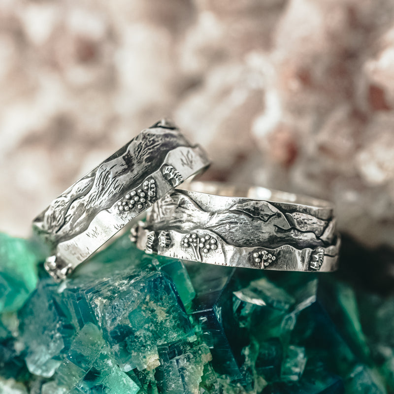 The White Mountains of New Hampshire mountain line on a sterling silver ring. Both rings are shown on a piece of dark green mineral stone. 