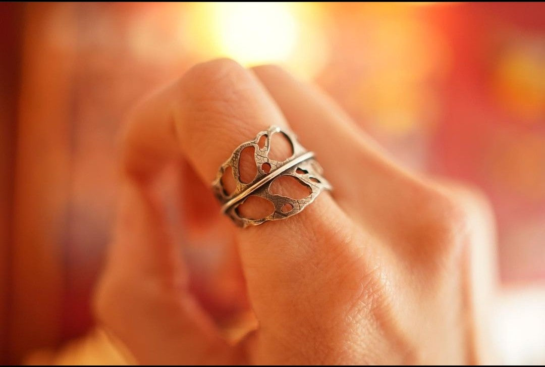 A hand is shown wearing a sterling silver monstera obliqua ring with a soft focus on the background. 