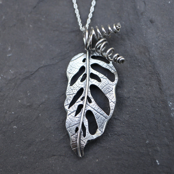 Handmade sterling silver monstera adansonii necklace shown on a black rock with twisted stems.