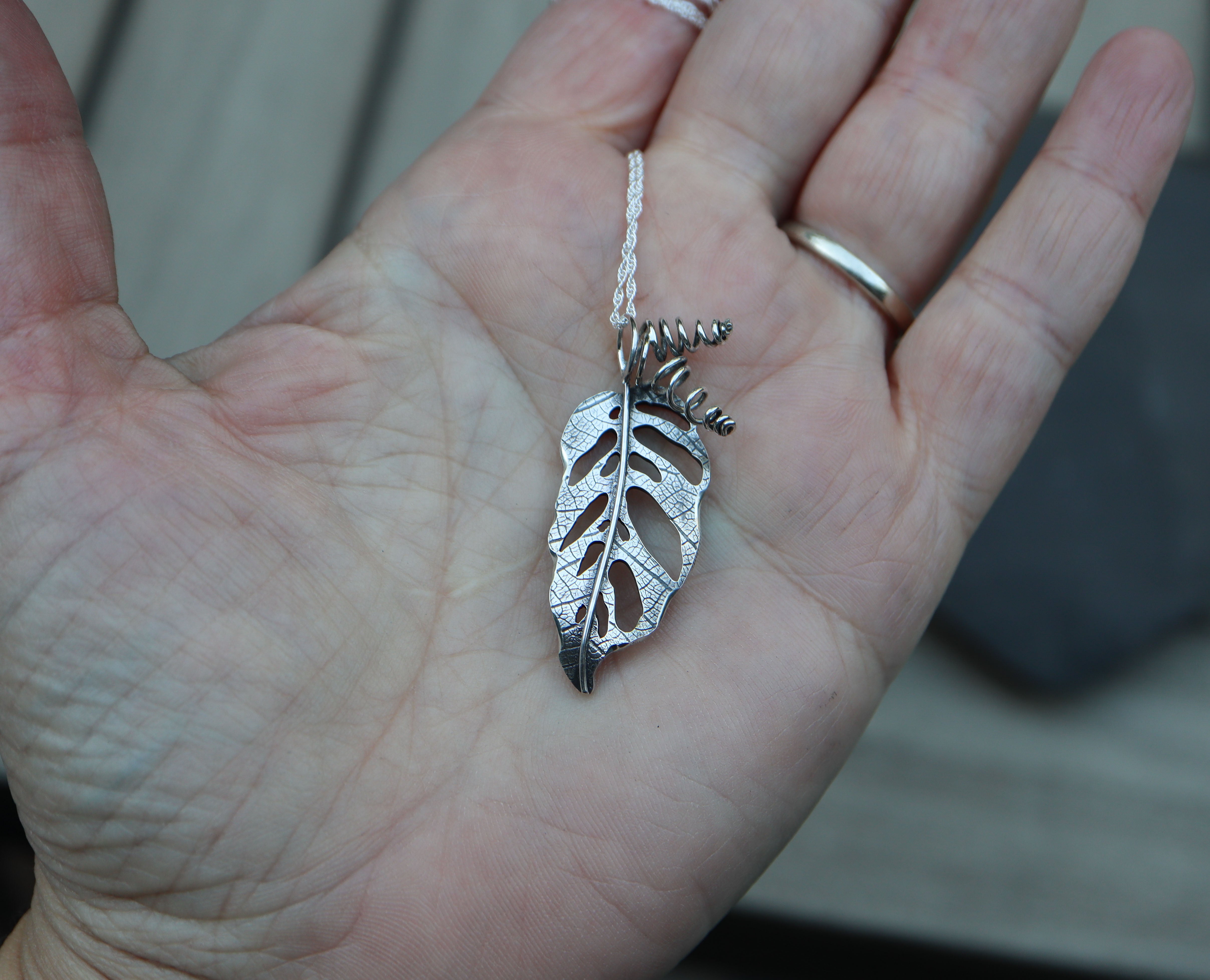 a handmade sterling silver monstera adansonii leaf pendant shown in someone's hand for size scale