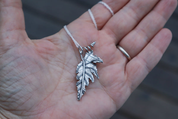 A hand holding a sterling silver handmade begonia leaf necklace made by The Striped Cat Metalworks