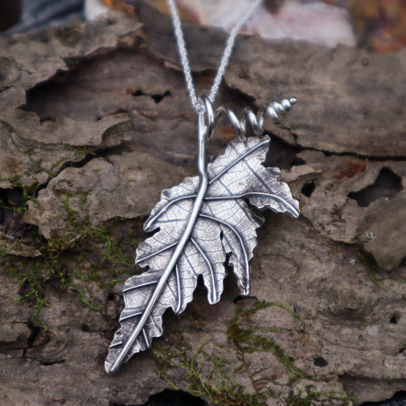 A sterling silver angel wing begonia leaf necklace shown on a piece of tree bark made by The Striped Cat Metalworks.