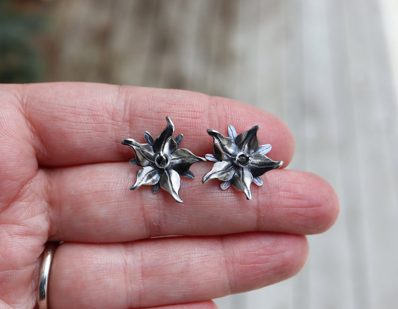 Silver borage flower earrings shown being held in a hand for size reference. They are about 1 inch tall. 