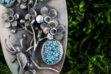 A close up view of one of the blue spotted turquoise stones. They are a sky blue color. Above the stone are a few of the forget-me-not-flowers. 