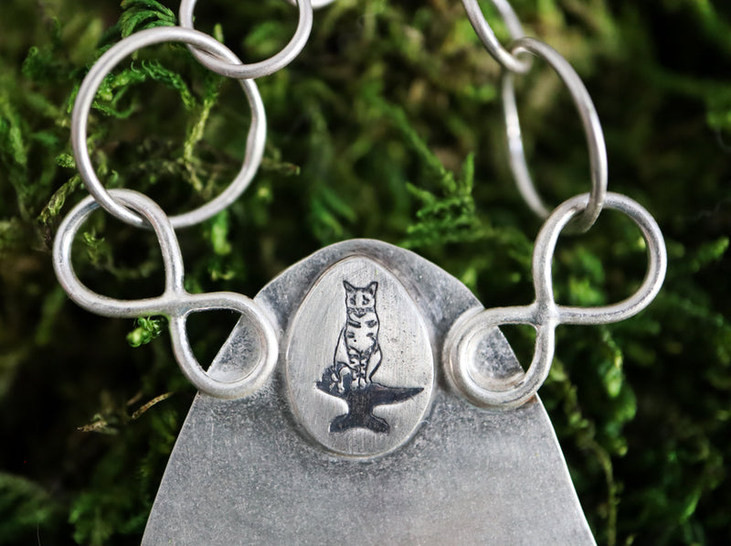 A close up photo of my maker's mark of my striped cat Max sitting on an anvil with his tail curled up around his feet. 