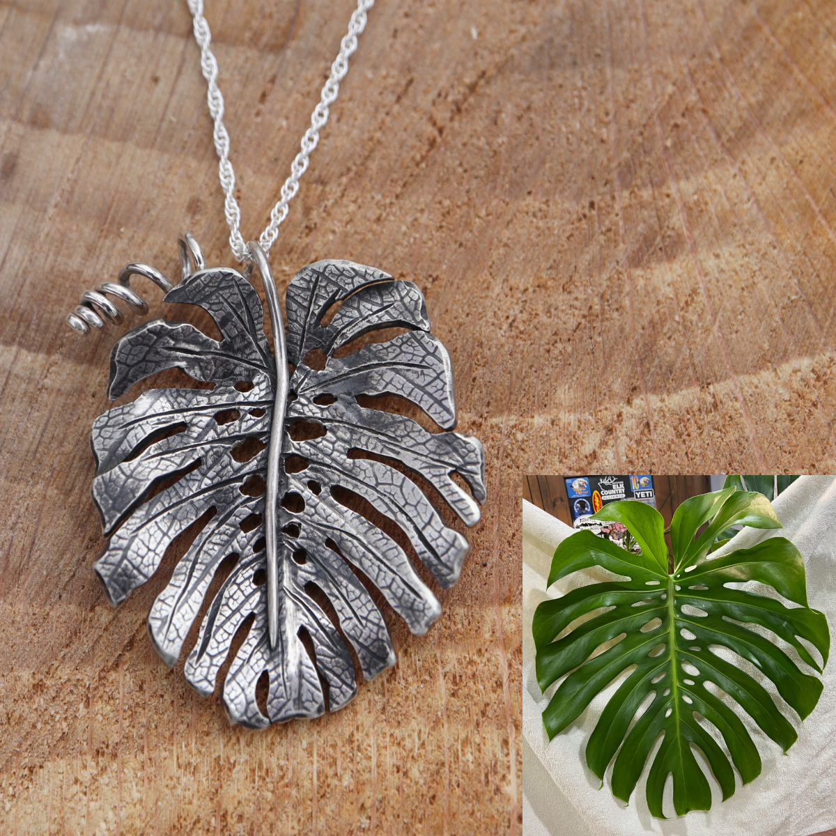 A custom made sterling silver monstera deliciosa necklace is shown on a piece of dark tan wood. 