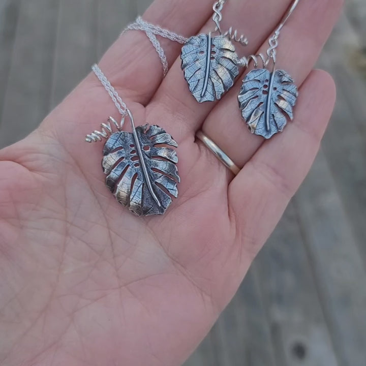A video showing what a matching set of monstera deliciosa earrings and necklace look like in someone's hand. 
