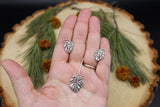 A hand is shown holding the matching monstera deliciosa stud earrings and matching necklace set.