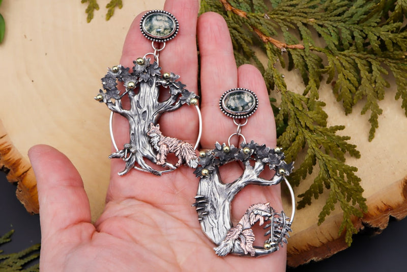 A hand is shown holding the mismatched fox hoop earrings for size. 