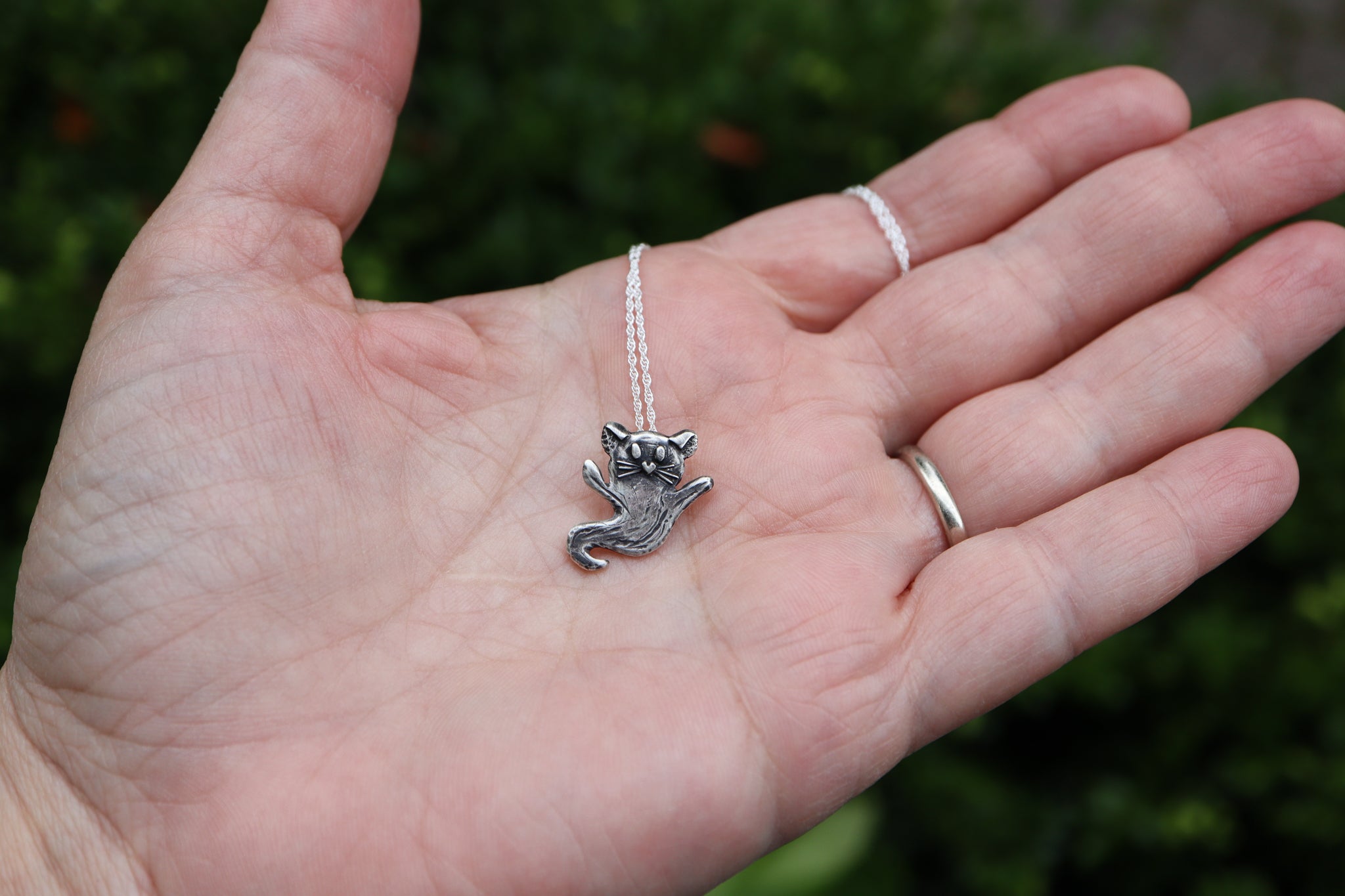 A hand is shown holding the sterling silver ghost cat for size reference. The cat is about .75 inches tall. 