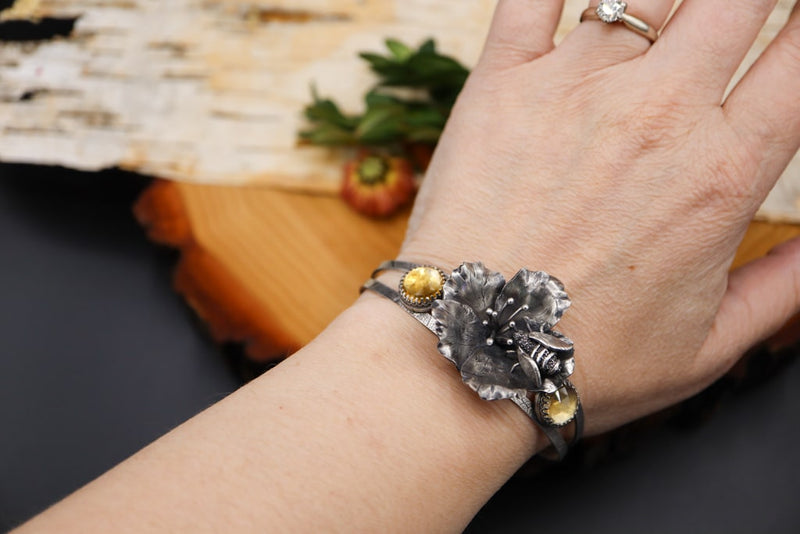 A hand is shown wearing the honey bee and flower blossom bracelet. 