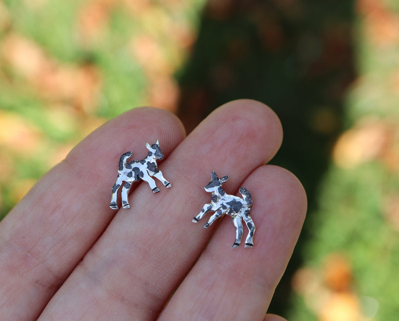 A hand is shown holing the small sterling silver goat stud earrings for size reference. They are about 1/2 inch wide. 