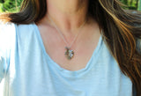 Someone is wearing a blue shirt wearing a silver monstera necklace.