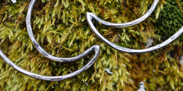 A close up of the hand hammered texture and oxidation given to the crescent moon earrings. They are shown on some real moss. 