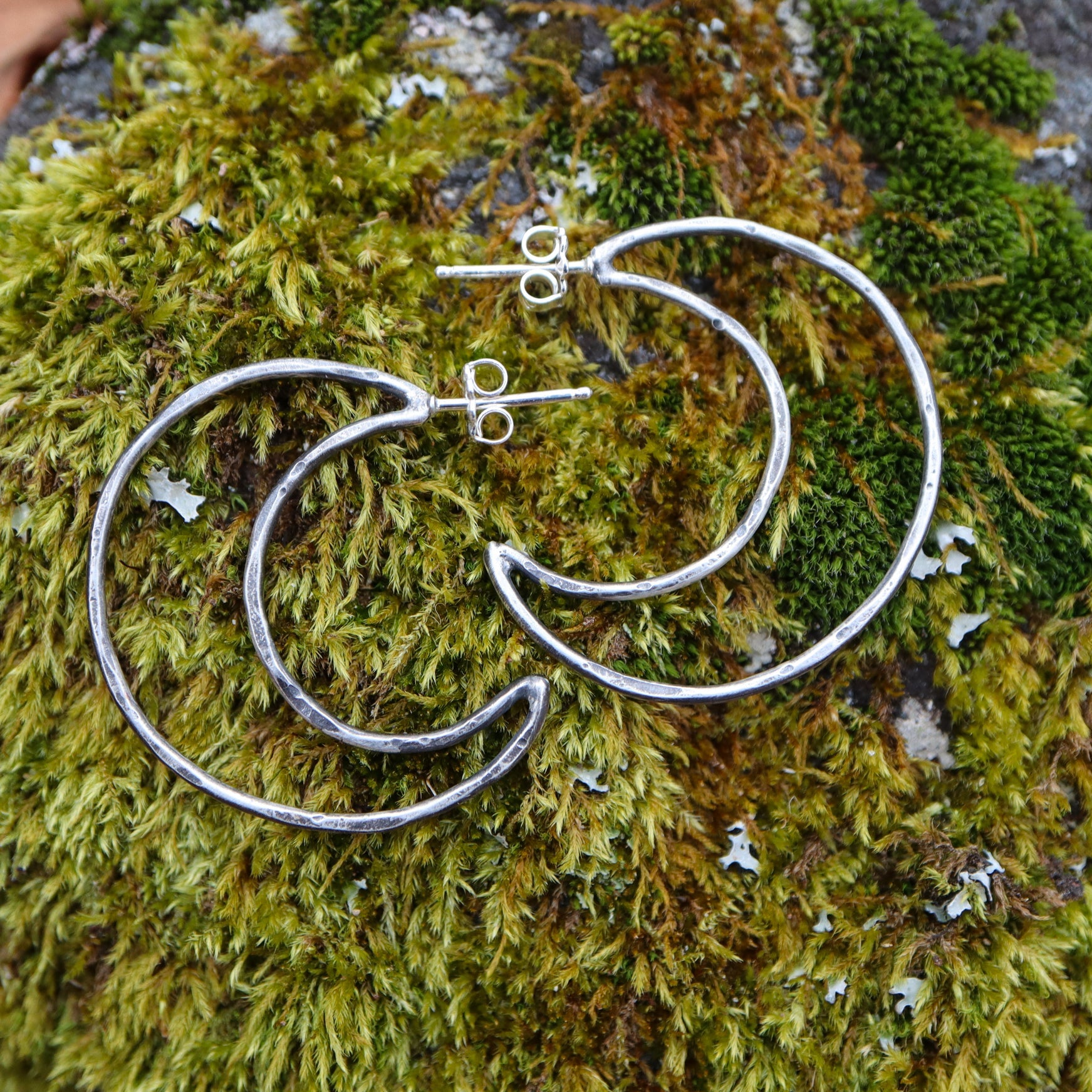Handmade sterling silver crescent hoop earrings are about 1.25 inches tall and shown on some real moss. 