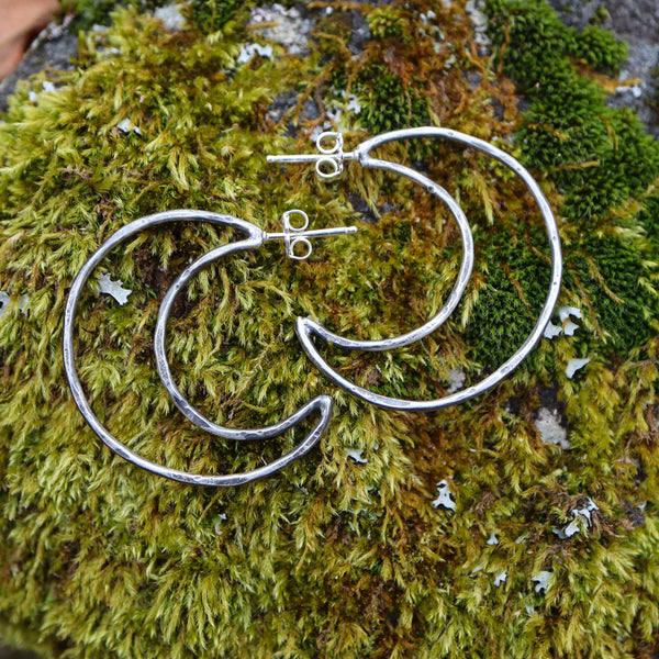 Handmade sterling silver crescent hoop earrings are about 1.25 inches tall and shown on some real moss. 