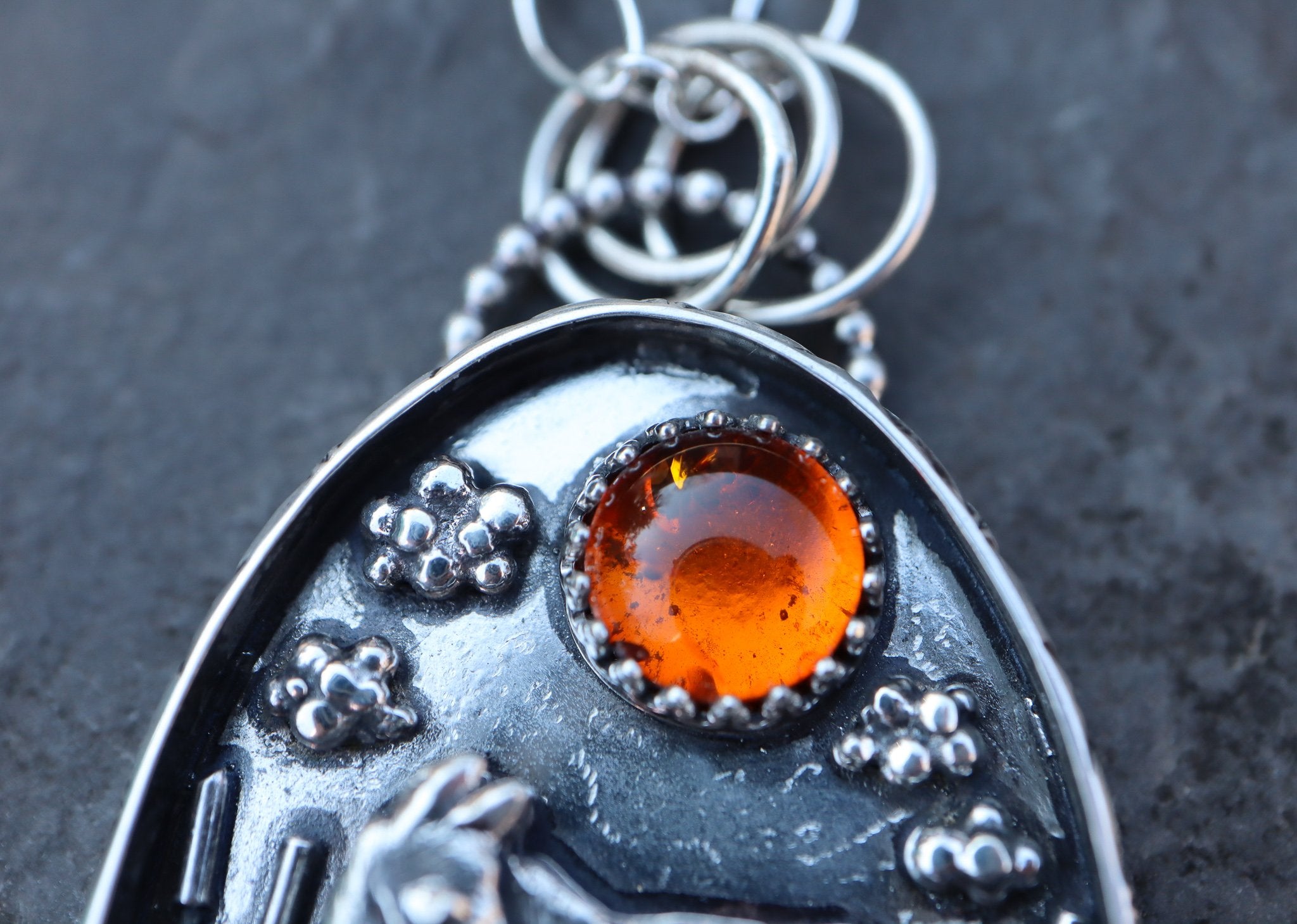 A close up of the natural amber gemstone at the top of a handmade moose pendant created by The Striped Cat Metalworks. 