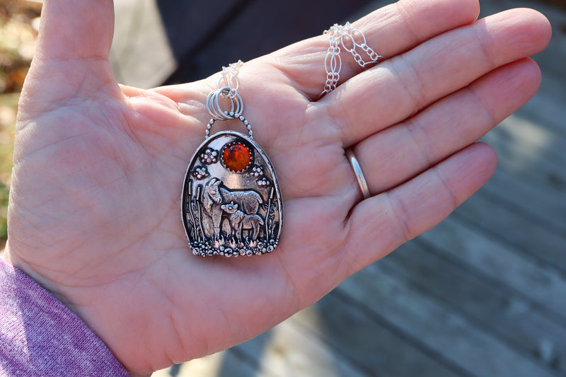 A handmade mother and child moose pendant shown in someone's hand to show the pendant's size. Made by The Striped Cat Metalworks.