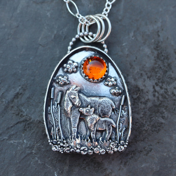 The Striped Cat Metalworks created a one of a kind sterling silver moose pendant with a mother and baby moose shown in a grassy swamp all made from sterling silver with a natural amber stone.