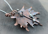 A close up of the three silver mushrooms on the copper maple leaf. The leaf is shown on a piece of dark grey stone slate. 