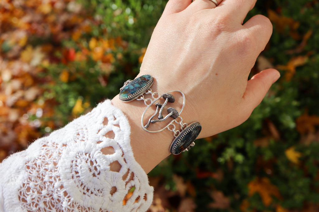 A hand is shown wearing the mushroom bracelet with opalized petrified wood cabochons. 