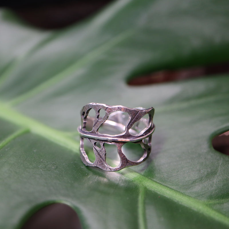 Sterling silver monstera obliqua ring shown on a green plant leaf.