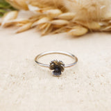 A single sterling silver pansy flower ring is shown on a light tan piece of wood. 