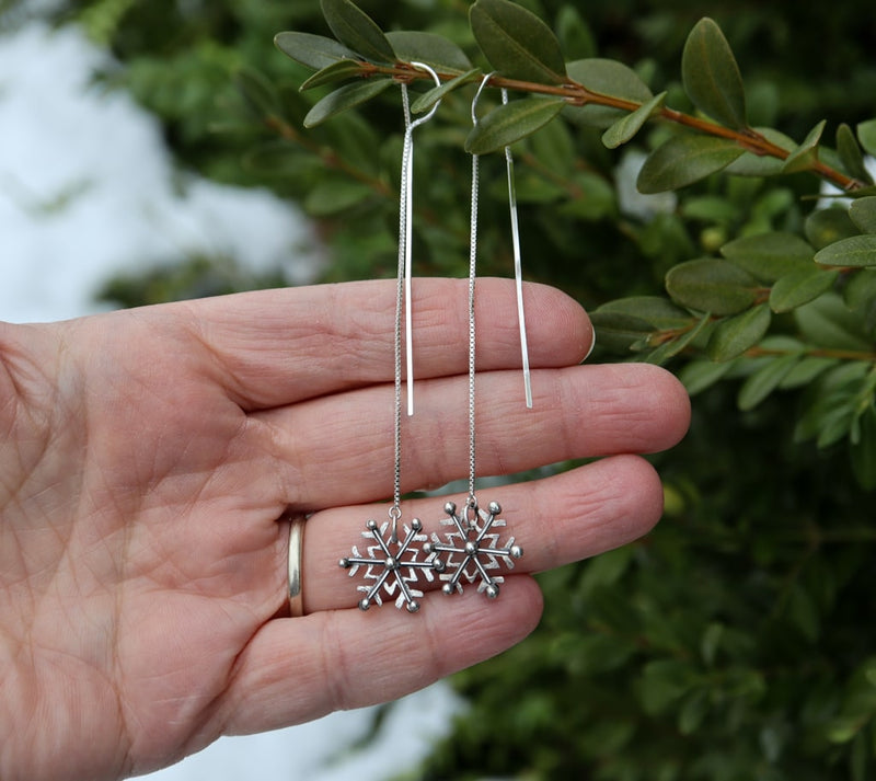 The sterling silver snowflake earrings are shown on a hand for size reference. They are about 6 inches long.