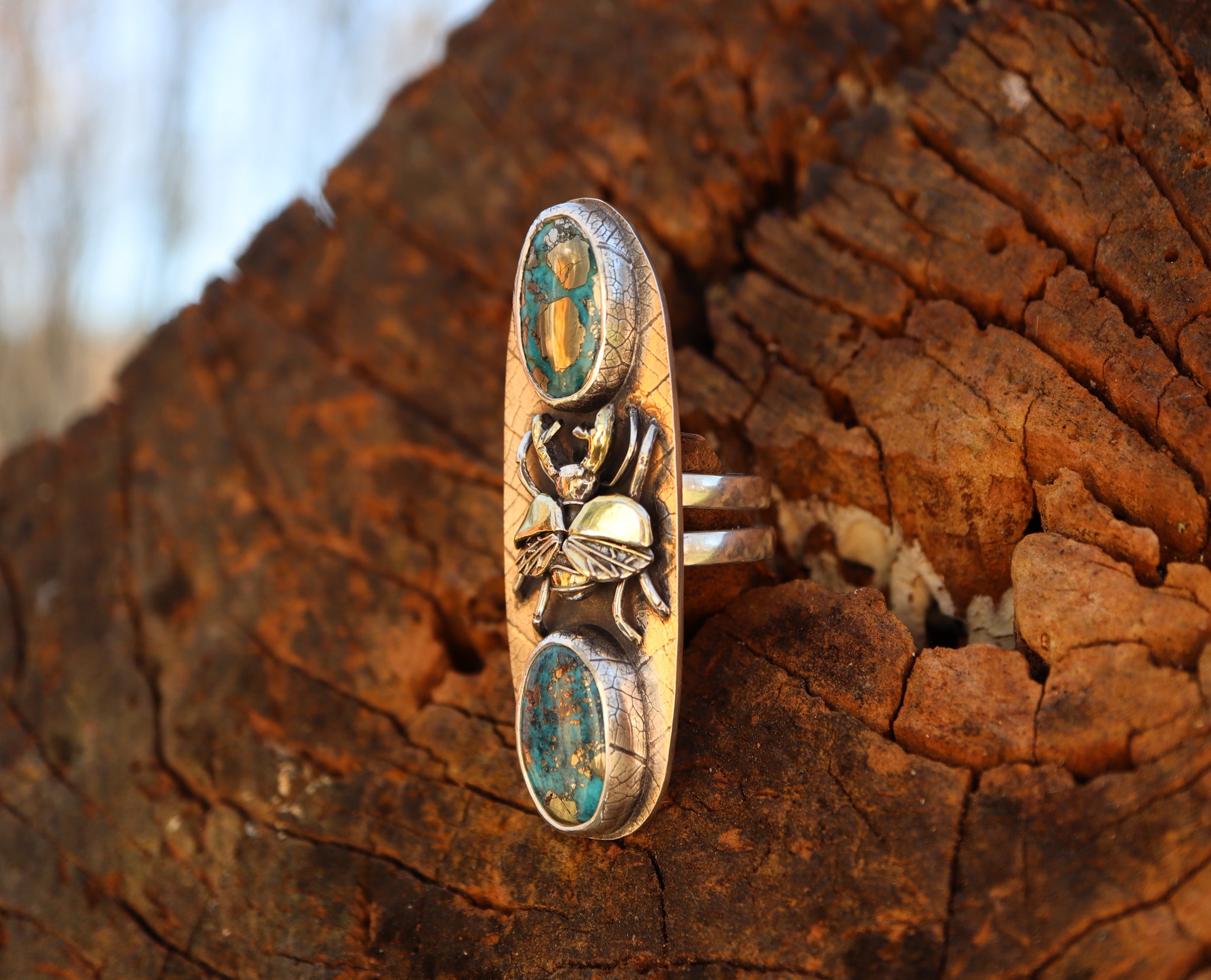 A side view of the silver and gold stag beetle ring. It shows the double ring band and the leaf patterned bezels holding the morenci turquoise stones. 