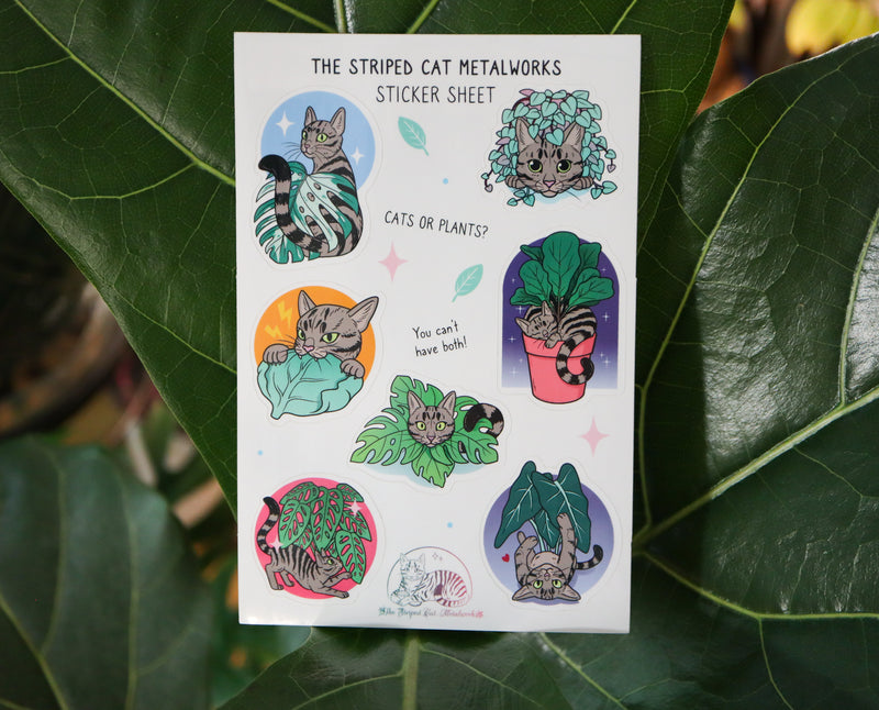 The Striped Cat Metalworks sticker sheet featring MAx the striped cat and houseplants like a fiddle leaf fig, monstera adansonii, monstera albo, string of hearts, and an alocasia polly all being played with by Max the cat! The stickers are shown on a real fiddle leaf fig plant.