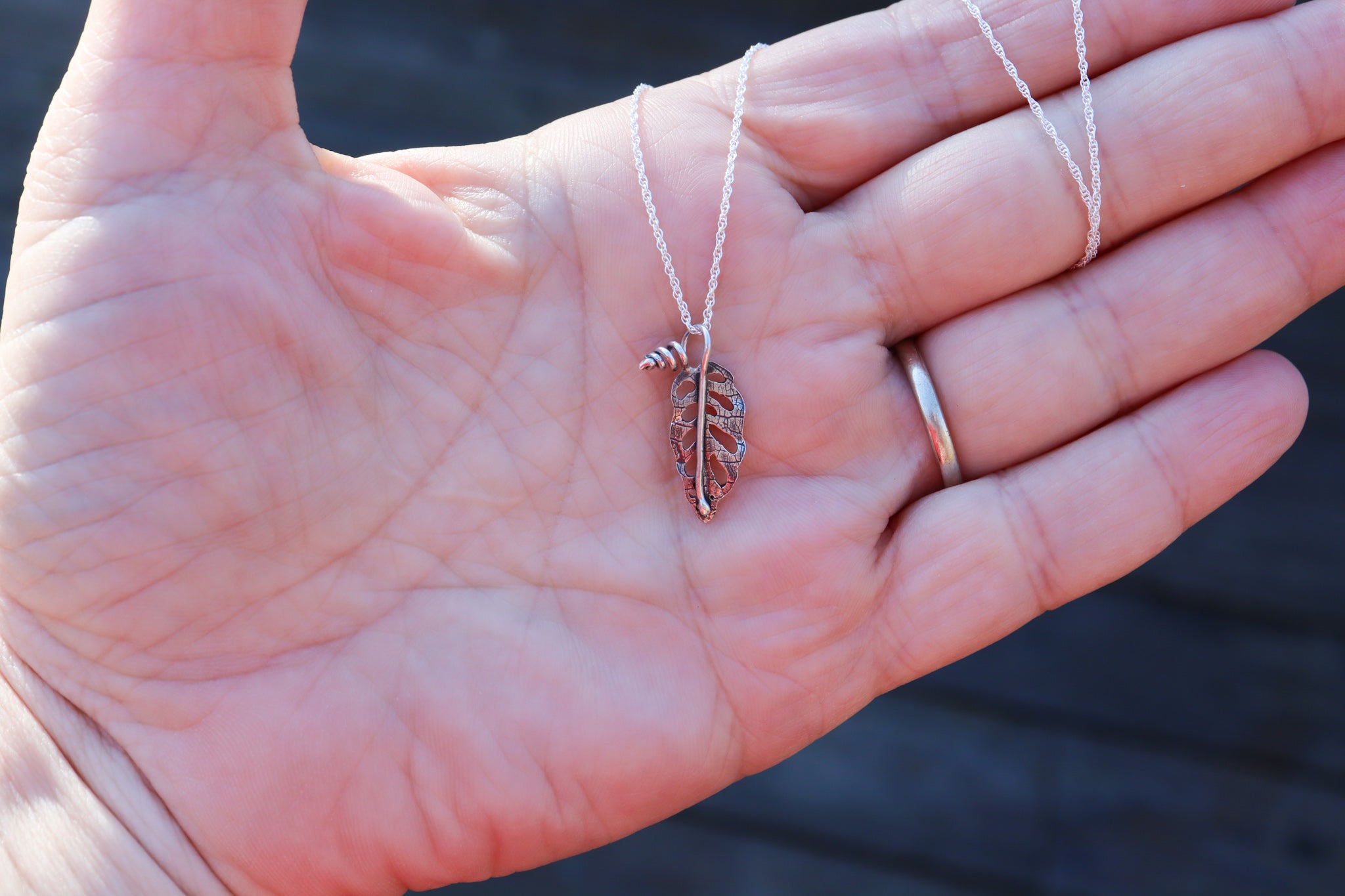 A hand holding a small monstera adansonii pendant that was handmade by The Striped Cat Metalworks. It is being held in a hand to show size. 