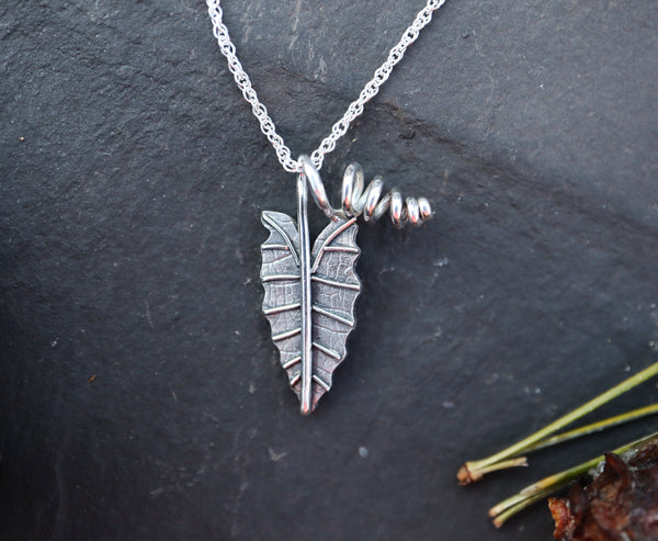 A small sterling silver alocasia polly necklace shown on a dark grey slate. 