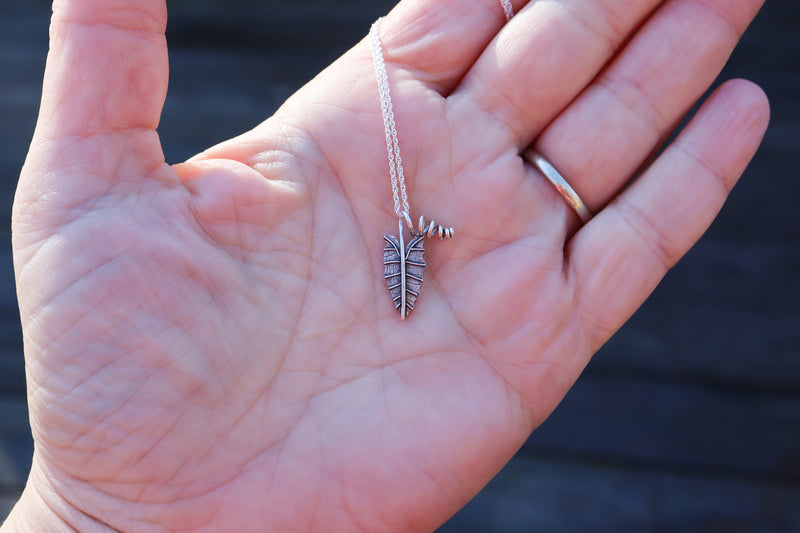 A hand holding a small sterling silver handmade alocasia polly pendant. 