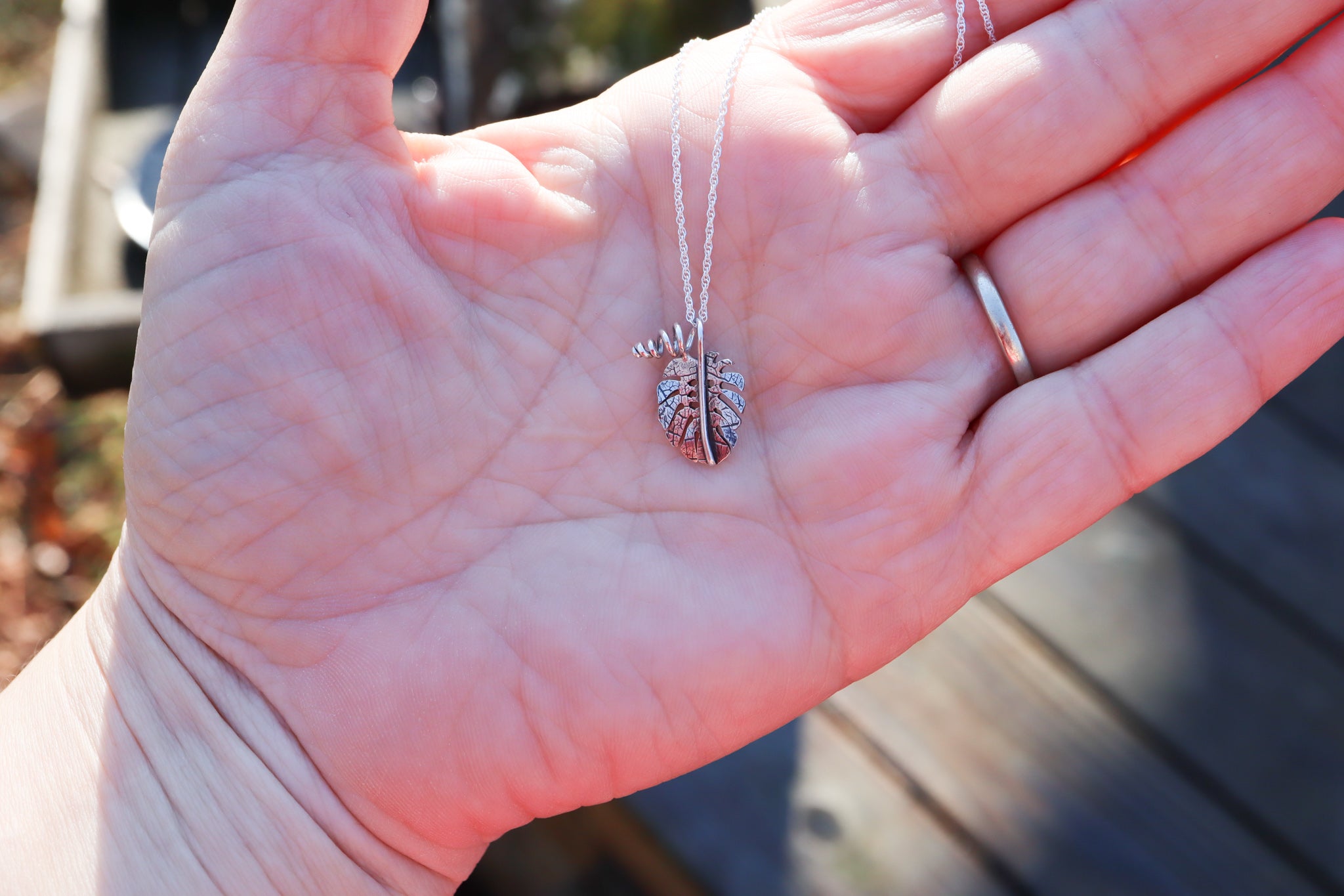 A small sterling silver monstera deliciosa necklace being shown in someone's hand for size scale.