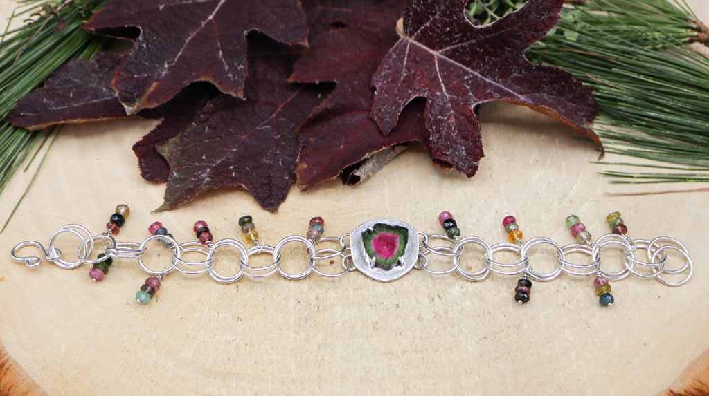 This is the bracelet outstretched showing all of the colors. There are dark red leaves and pine needles above the bracelet. 